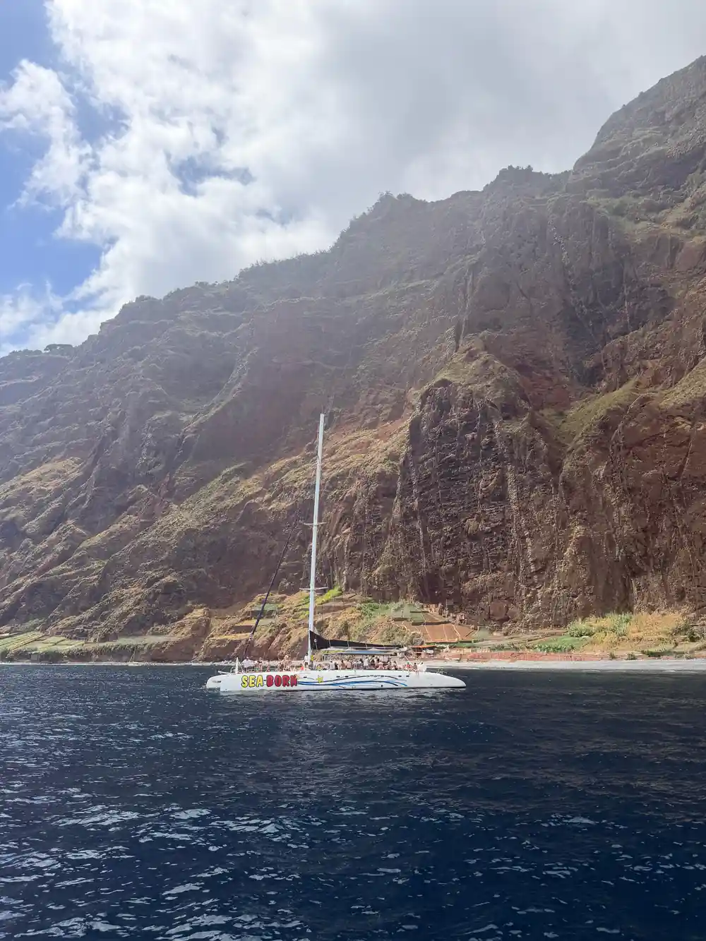 The catamaran anchored below a massive cliff face