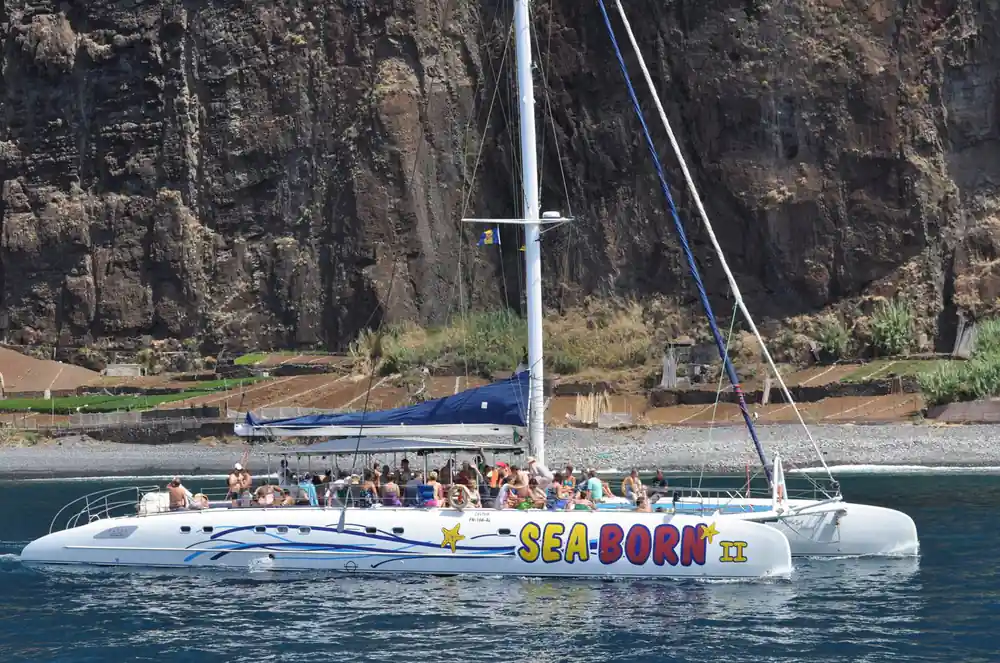 The Sea-Born catamaran crowded with guests below a tall cliff