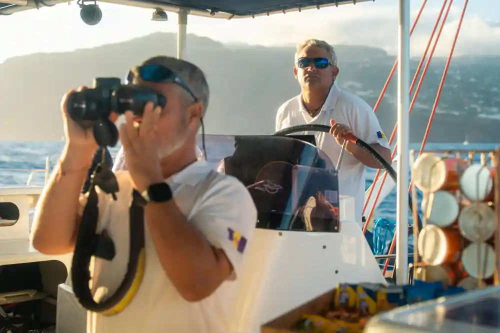 The skipper at the wheel with a guest photographing beside him