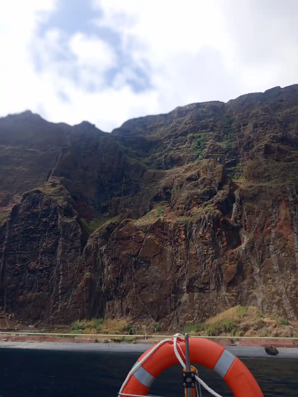 A steep rock face and green slope rising from the sea