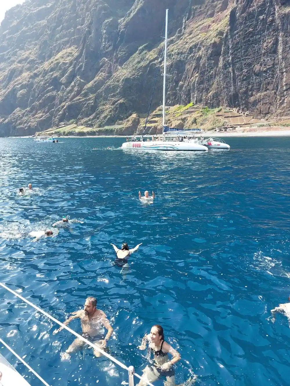 Swimmers in clear blue water beside the anchored catamaran