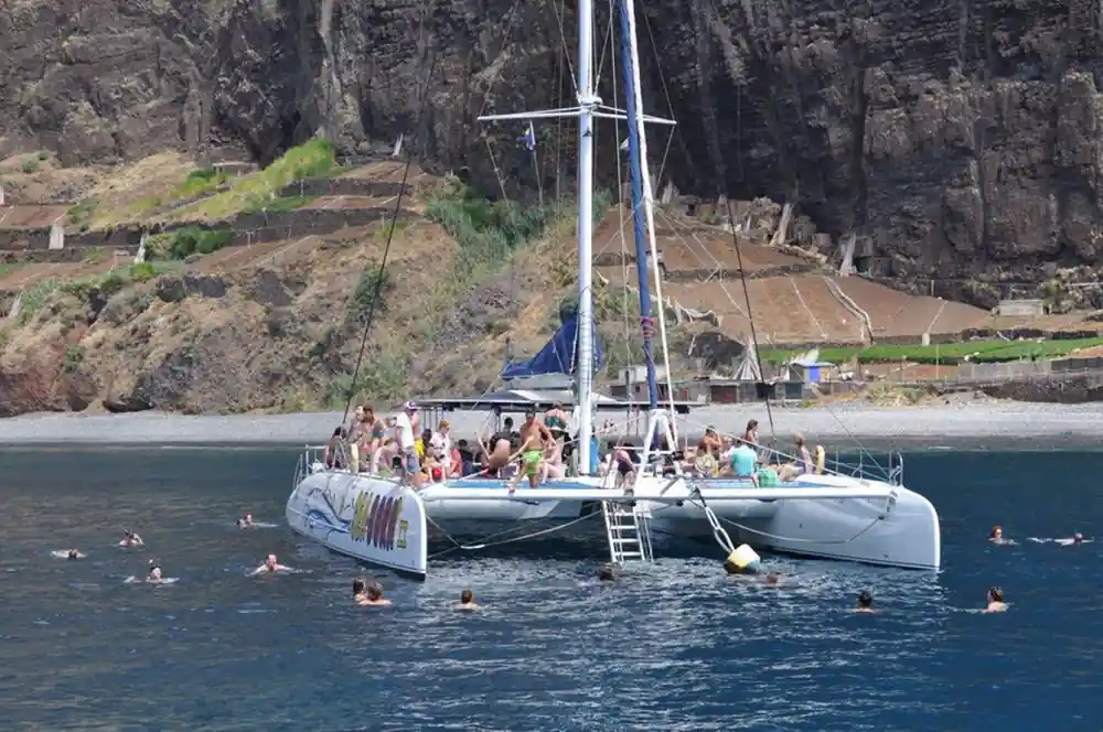 Swimmers in the water beside the catamaran below the cliffs
