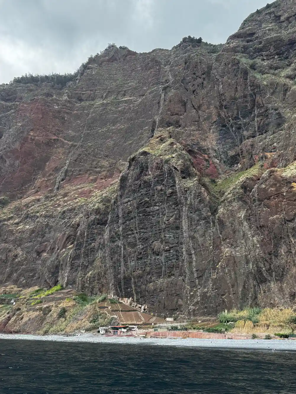 A tall red-brown cliff face above a narrow shore
